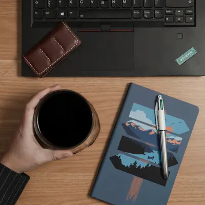 Gros plan sur un bureau avec un ordinateur, un bloc note, un stylo et une main tenant une tasse de café pendant une session de copywriting