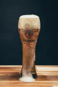 Verre de bière blanche avec la mousse de la bière qui coule tout autour du verre