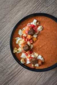 Bol de gaspacho décoré d'oeuf, de tomates fraiches, de fromage de chèvre et de croûtons